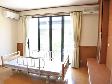 木の風合いが漂う小さなワンルームタイプの部屋の様子。エアコン、収納、介護用ベッドなどが置いてある様子