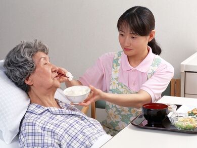 ベッドに寝た状態で食事を摂っている女性と介助しているスタッフの様子